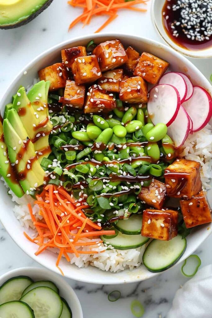 Das Bild zeigt eine weitere leckere Bowl, die ebenfalls eine Mischung aus frischen Zutaten und gesunden Komponenten enthält. In dieser Bowl findest du Tofu, Reis, edamame Bohnen, Avocado, Radieschen, Karottenstreifen, Frühlingszwiebeln und Gurken. Alles ist mit einer leckeren Sauce überzogen und mit Sesamsamen bestreut. Die Kombination aus verschiedenen Texturen und Aromen macht diese Bowl besonders ansprechend. Dies ist ein weiteres tolles Beispiel für ein vegetarisches oder veganes Gericht, das sich gut für Buffets eignet, besonders für Gäste, die nach gesunden, pflanzlichen Optionen suchen. Die Vielfalt an Gemüse und Proteinen sorgt für ein ausgewogenes und nährstoffreiches Essen.